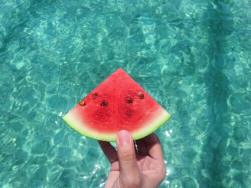 Eine Hand, die ein Stück Wassermelone über einem Pool hält.